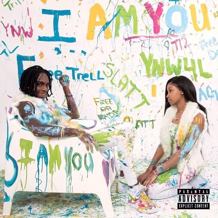 Melly' album I AM YOU is Melly sitting on a white chair with a girl also in white kneeling in front of him. they are splashed with paint 